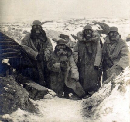 Vier deutsche Soldaten in Pelzmänteln und Gasmasken in einem Schützengraben, 1917